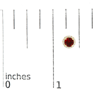 Close-up of a round yellow metal earring with a red gemstone center surrounded by small white gemstones, shown on a scale.