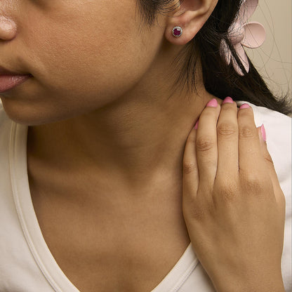Close-up side view of a model wearing a yellow metal round earring featuring a red gemstone center surrounded by small white gemstones in a shared prong setting.