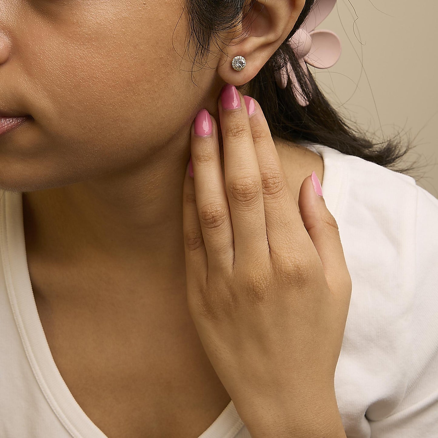 Close-up angled view of a model wearing a round yellow metal stud earring featuring a white gemstone center surrounded by smaller white gemstones.