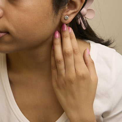 Close-up angled view of a model wearing a round yellow metal stud earring featuring a white gemstone center surrounded by smaller white gemstones.