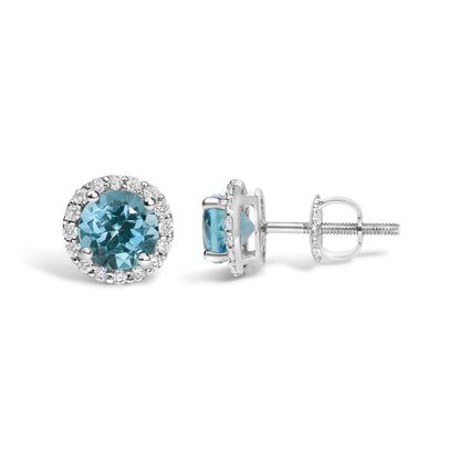 Pair of white metal stud earrings shown from front and side angles, each featuring a round blue gemstone in a four-prong setting surrounded by a halo of small round white gemstones in a shared prong setting.