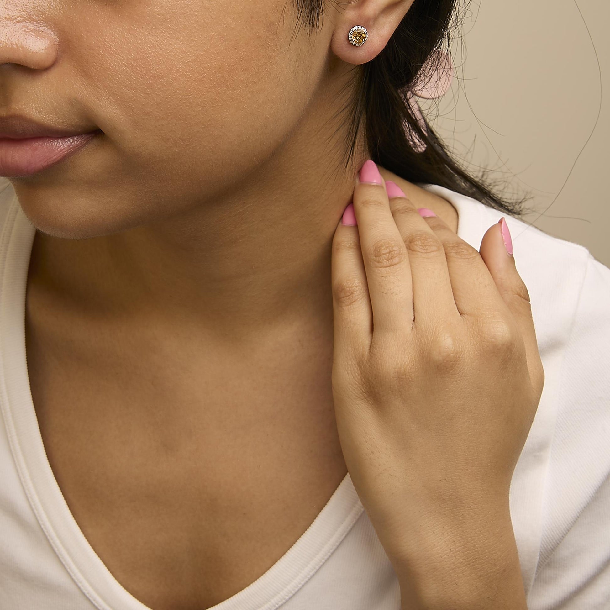 Close-up side angle of a model wearing white metal stud earrings featuring a round orange gemstone center surrounded by small round white gemstones in a shared prong setting.