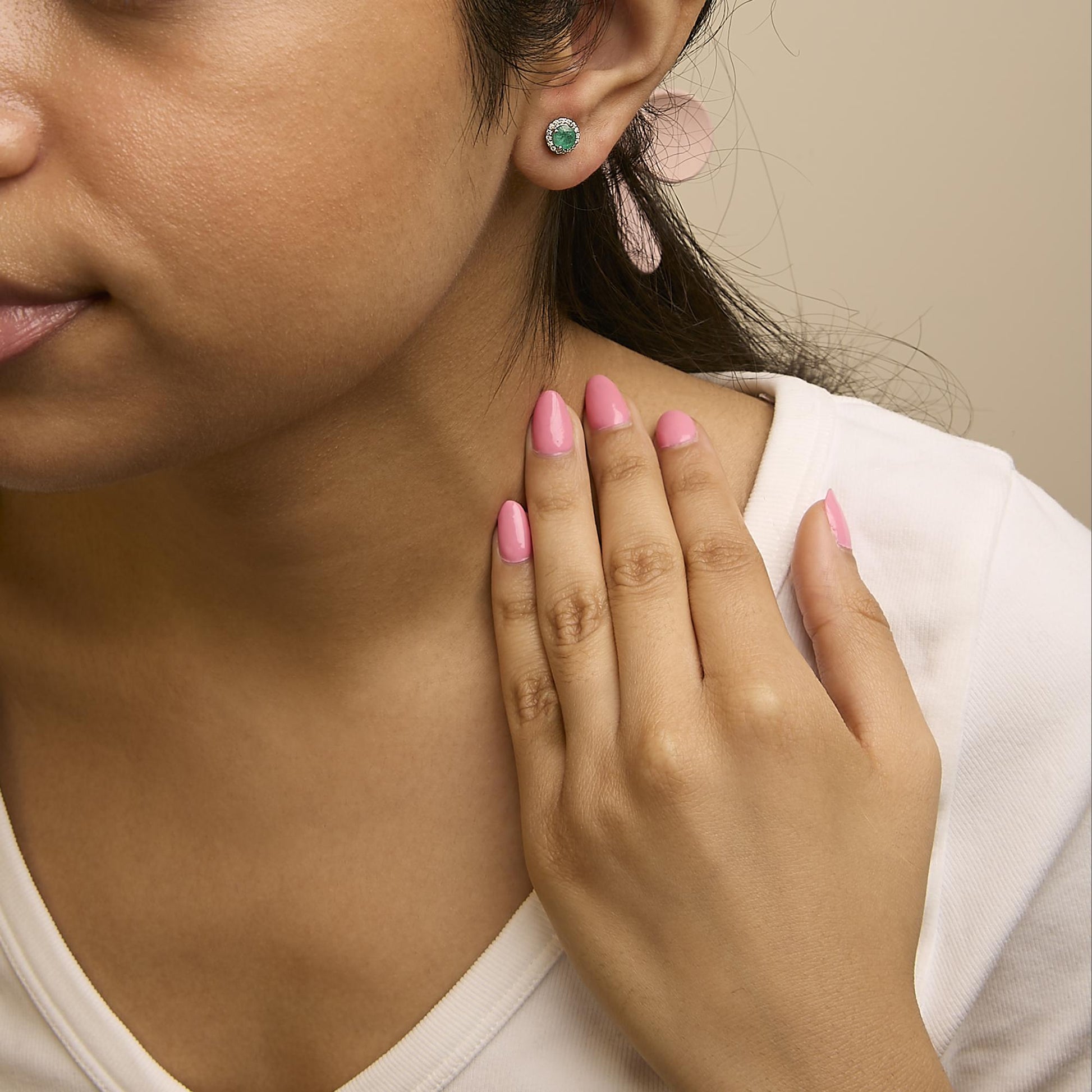 Close-up side view of a model wearing white metal round stud earrings featuring a central round green gemstone surrounded by a halo of small round white gemstones in shared prong settings.
