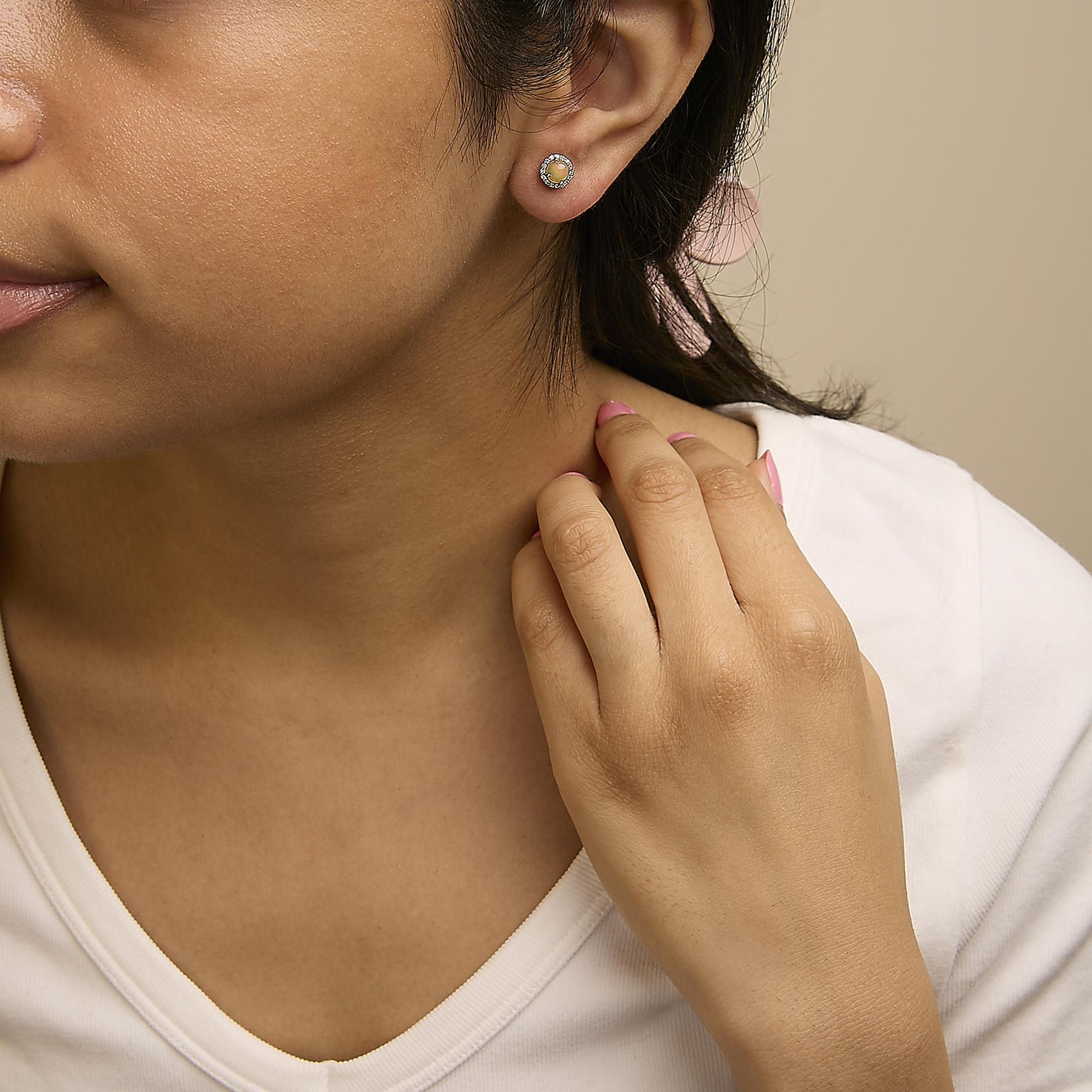 Close-up side view of a model wearing white metal round stud earrings with a central multi-color round gemstone surrounded by small white round gemstones in a shared prong setting.