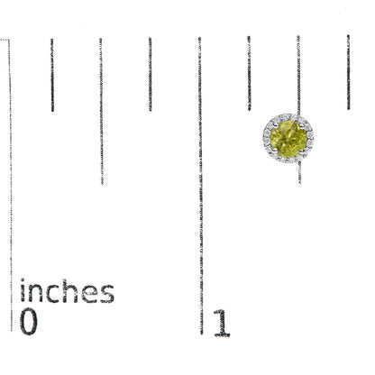 Single white metal round earring shown on a scale, featuring a central round green gemstone in a prong setting, surrounded by small round white gemstones in a shared prong setting, viewed from the front.