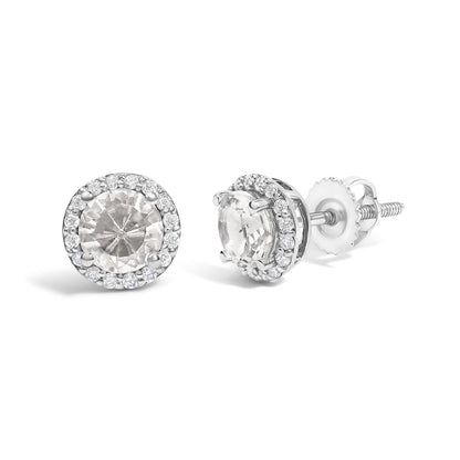 Pair of white metal stud earrings with round white gemstones in 4-prong settings surrounded by a halo of smaller round white gemstones in shared prong settings, shown from front and side angles on a white background.