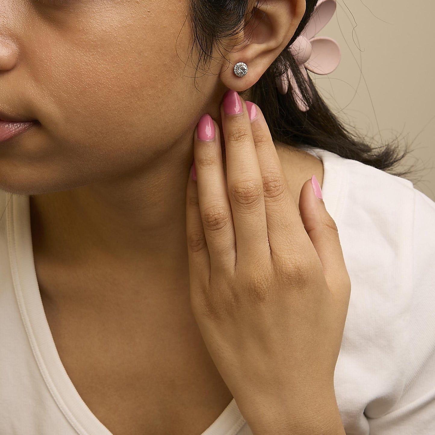Close-up side view of a model wearing round white gemstone stud earrings surrounded by smaller white gemstones in a shared prong setting, with the model's hand touching her ear.
