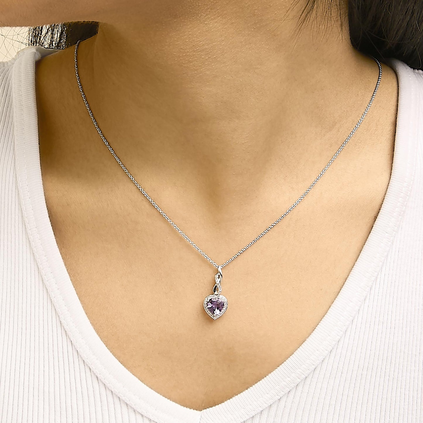 Set of jewelry shown worn on a model, featuring a necklace with a heart-shaped purple gemstone pendant surrounded by small white gemstones on a thin chain, shot from a frontal angle.