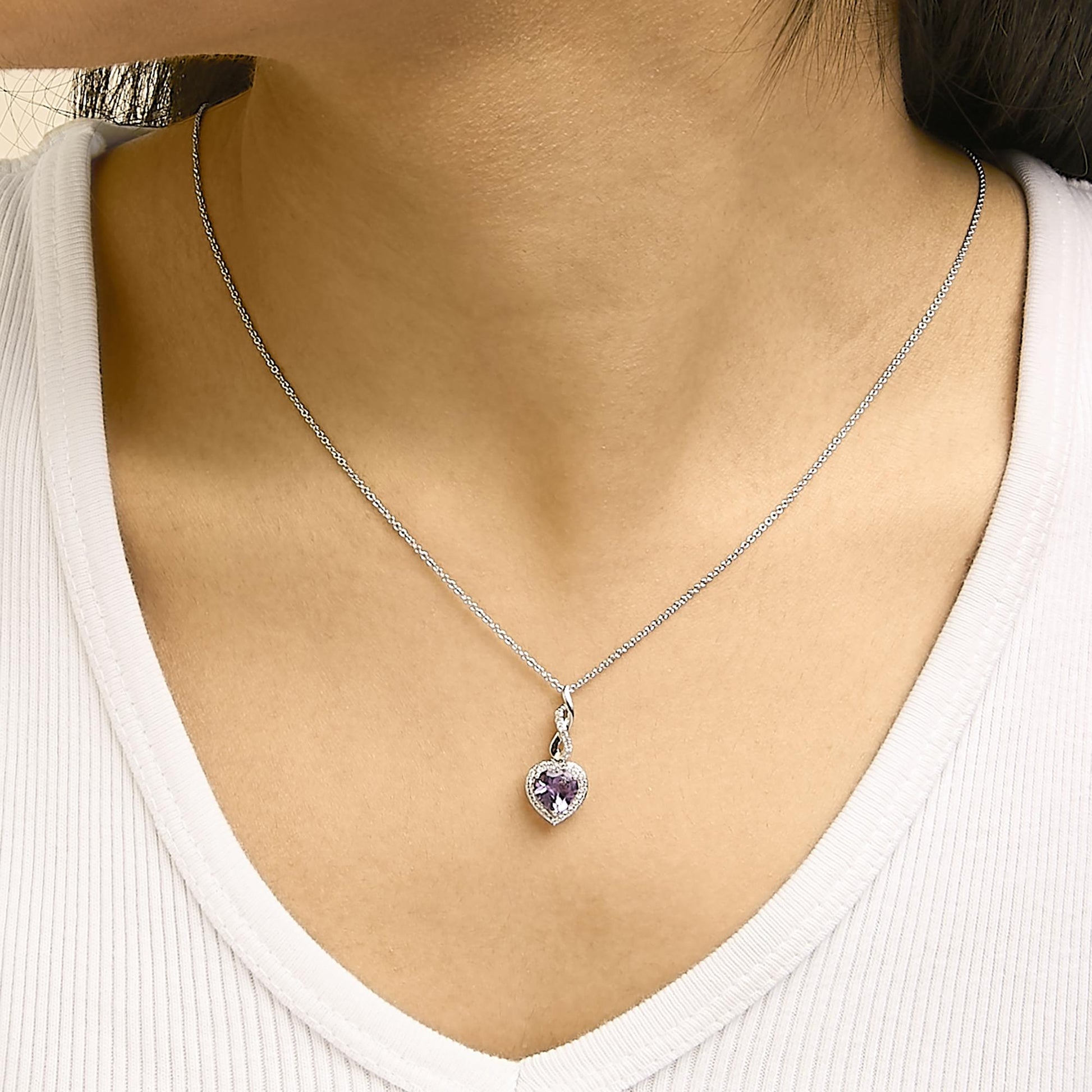 Set of jewelry shown worn on a model, featuring a necklace with a heart-shaped purple gemstone pendant surrounded by small white gemstones on a thin chain, shot from a frontal angle.