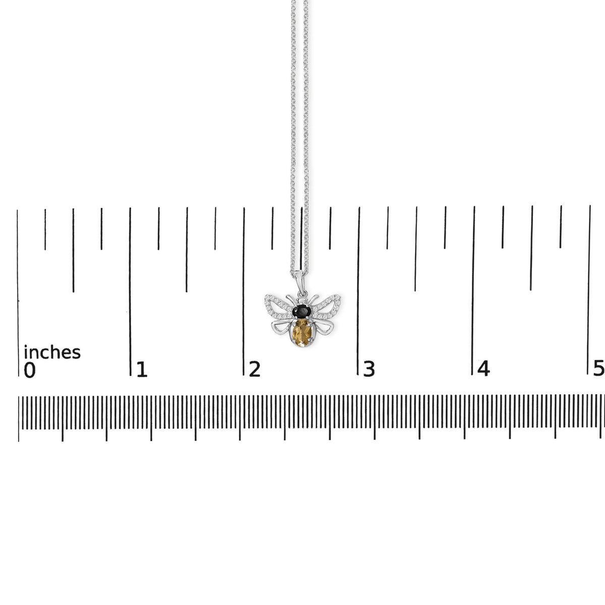 White metal necklace with a bee-shaped pendant adorned with one oval orange gemstone, one oval black gemstone, and multiple round white gemstones, shown on a ruler scale from a top-down angle.