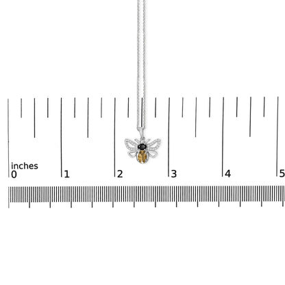 White metal necklace with a bee-shaped pendant adorned with one oval orange gemstone, one oval black gemstone, and multiple round white gemstones, shown on a ruler scale from a top-down angle.
