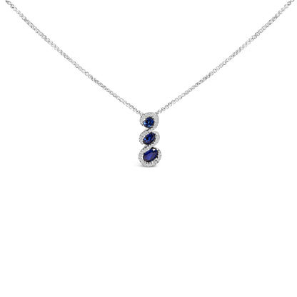 Front-facing view of a white metal necklace with a vertical pendant featuring three oval blue gemstones, each surrounded by small round white gemstones, shown on a white background.