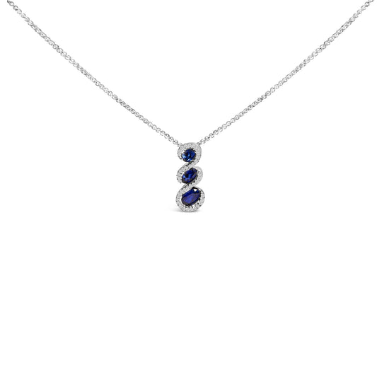 Front-facing view of a white metal necklace with a vertical pendant featuring three oval blue gemstones, each surrounded by small round white gemstones, shown on a white background.
