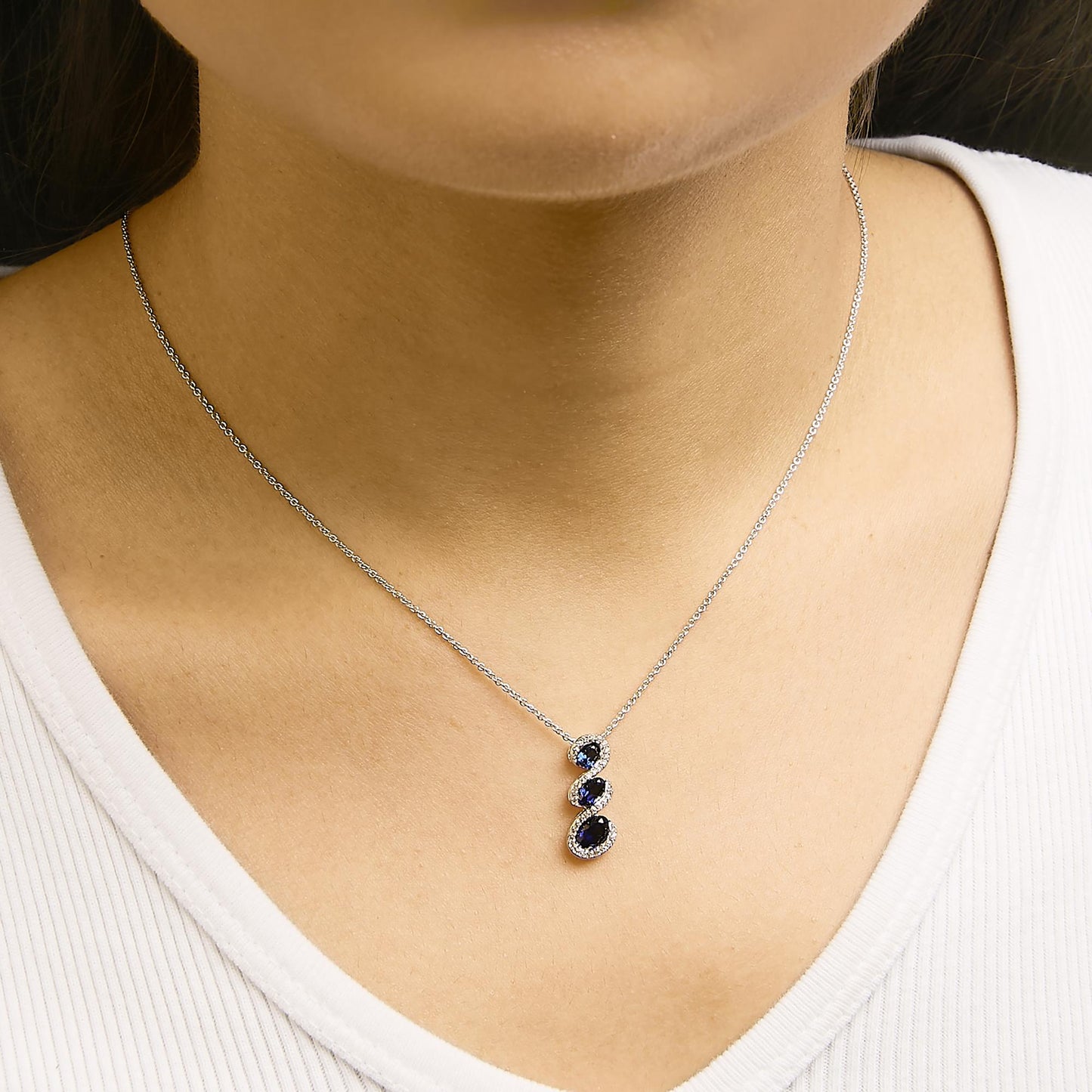 Necklace with three vertically aligned oval blue gemstones, each surrounded by small round white gemstones, shown worn on a model from the front angle.