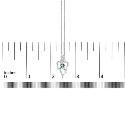 White metal angel-shaped necklace with a blue heart-shaped gemstone in the center and multiple small white round gemstones along the wings, shown on a scale.