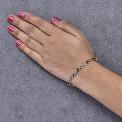 Yellow metal bracelet with alternating round, pear, oval, and emerald-shaped red, green, blue, and pink gemstones, and small round white gemstones, worn on a model's wrist, side angle view.