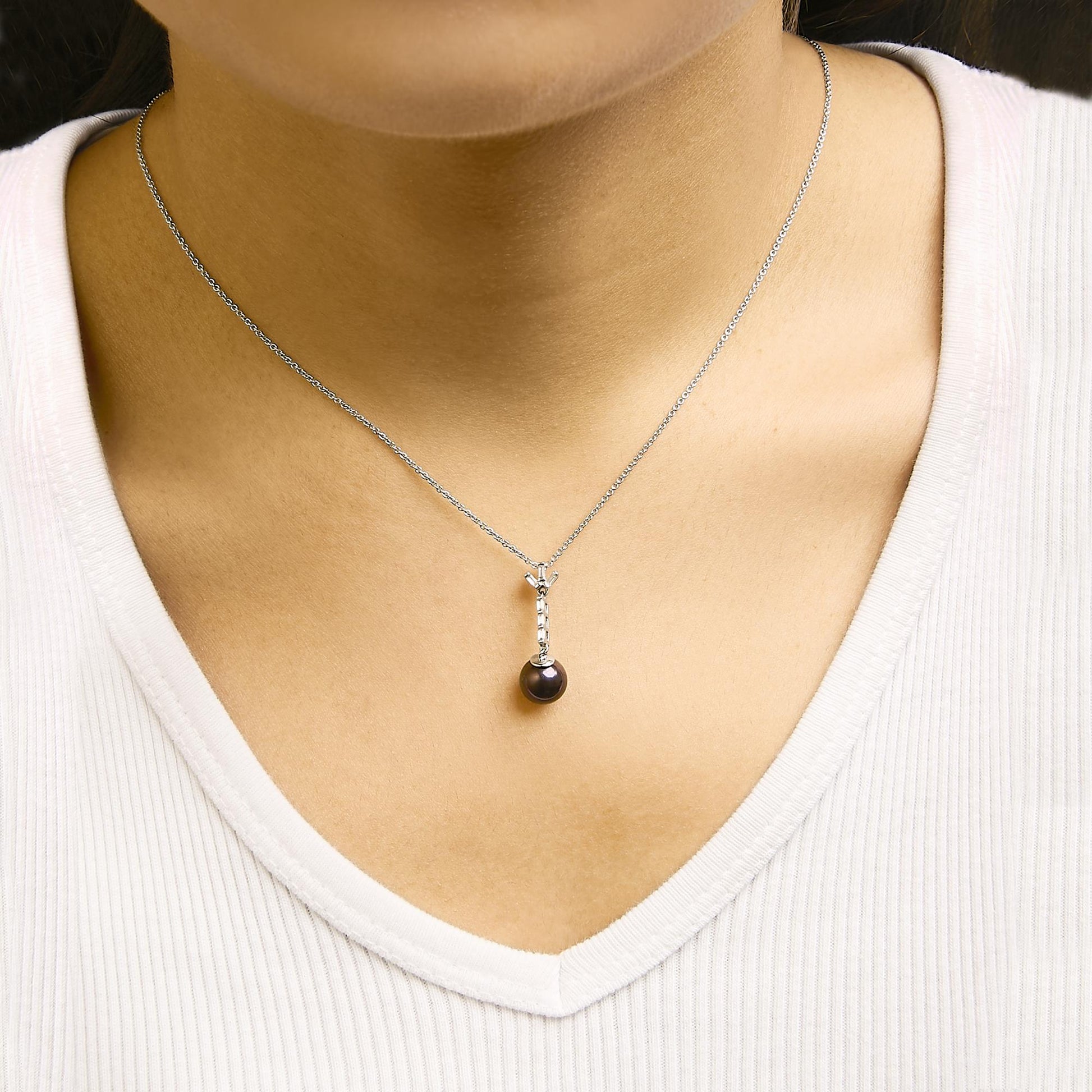 White necklace with a vertical bar pendant featuring six white baguette-shaped gemstones in channel setting, shown worn on a model, front close-up angle.