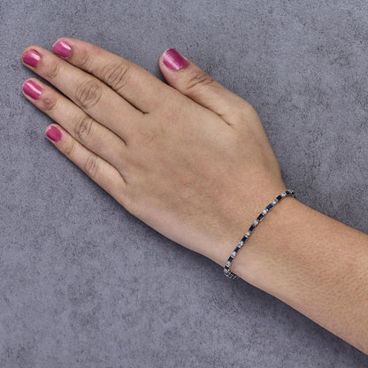 White metal bracelet with alternating round white gemstones in prong settings and blue baguette gemstones in channel settings, shown on a model's wrist from a top-down angle.