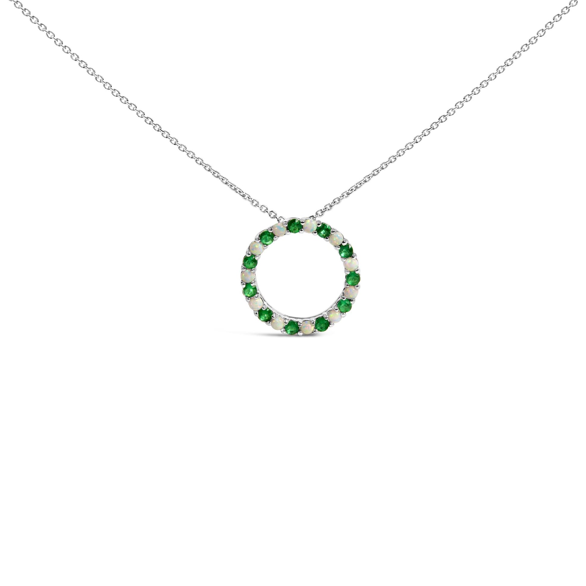 Front-facing shot of a white metal circular necklace pendant adorned with alternating round green and white gemstones in a shared prong setting.