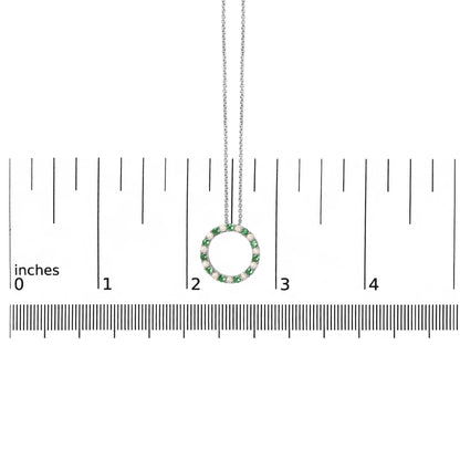 White metal circular necklace pendant with alternating green and white round gemstones in shared prong settings, shown hanging on a chain against a ruler scale from a front angle.