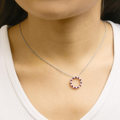 Necklace shown worn on a model, featuring a white metal circular pendant with alternating round red and white gemstones set in prong settings, shot from the front at close range.