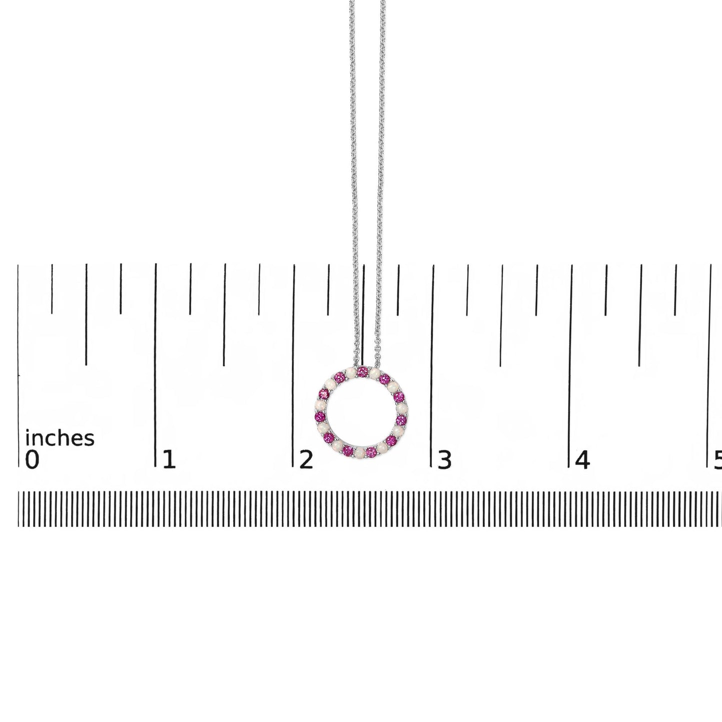 White metal circular necklace pendant featuring alternating round red and white gemstones in prong settings, shown hanging centered on a ruler scale from a front angle.