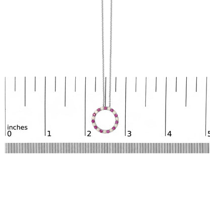 White metal circular necklace pendant featuring alternating round red and white gemstones in prong settings, shown hanging centered on a ruler scale from a front angle.