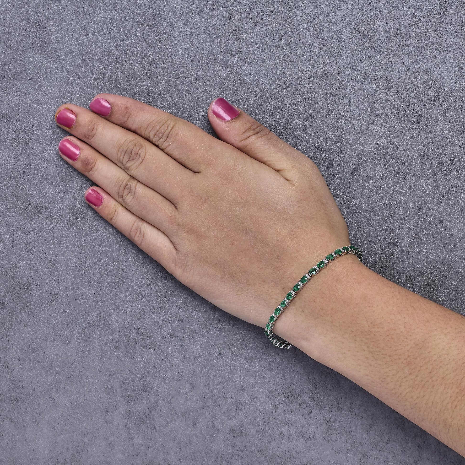 White metal bracelet with alternating green oval gemstones and white round gemstones in prong settings, shown worn on a model's wrist from a top-down angle.