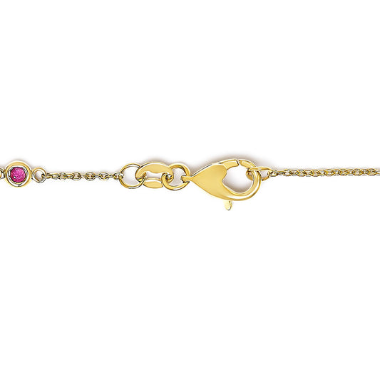 Close-up side angle of a yellow metal bracelet chain with a clasp and a round red gemstone in bezel setting.