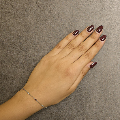 Close-up top view of a yellow metal bracelet with round bezel-set white gemstones and round bezel-set red gemstones, worn on a model's wrist.