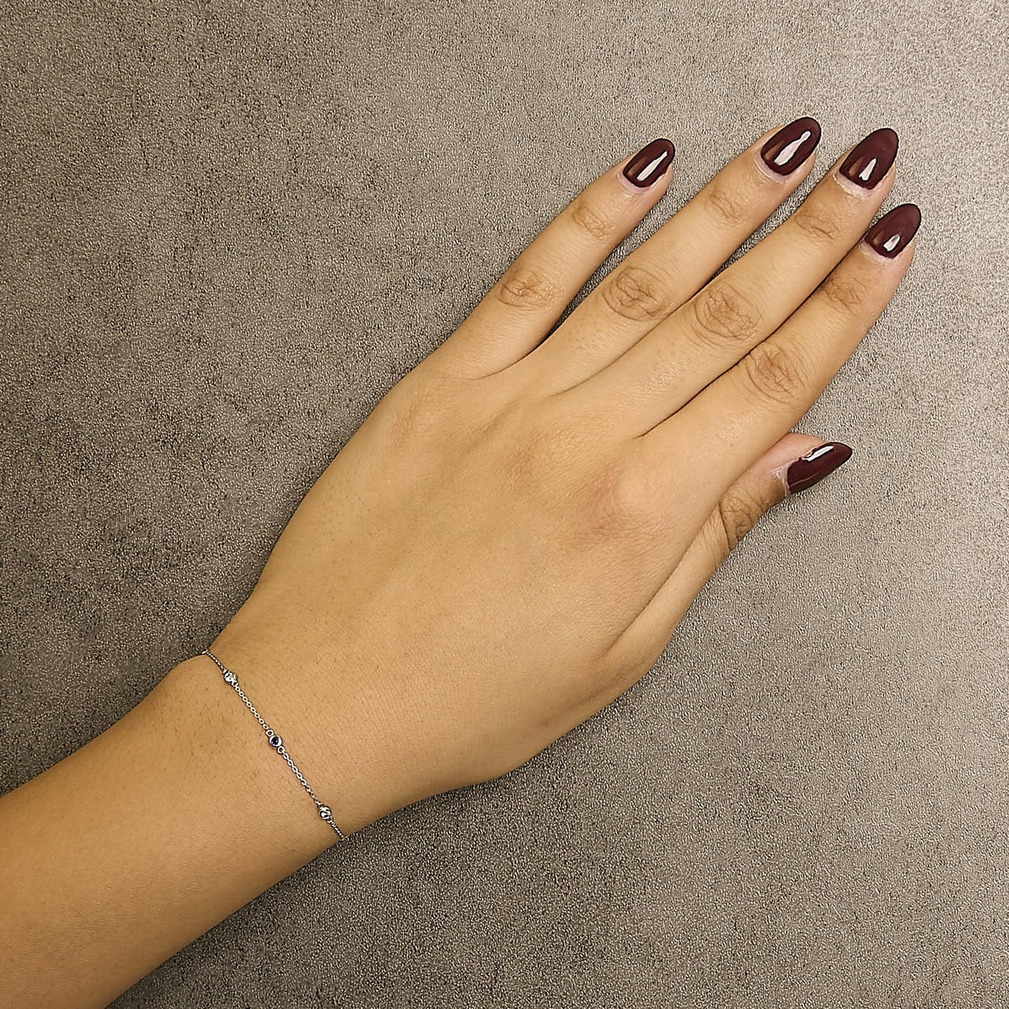 White metal bracelet with round bezel-set white and blue gemstones, shown on a model's wrist from above.