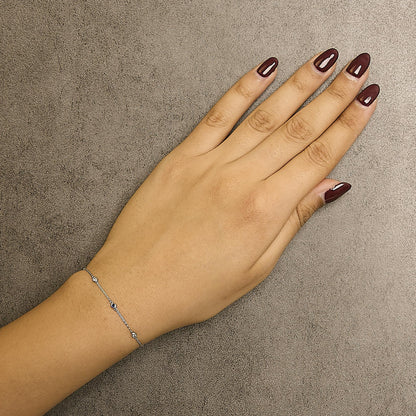 White metal bracelet with round bezel-set white and blue gemstones, shown on a model's wrist from above.