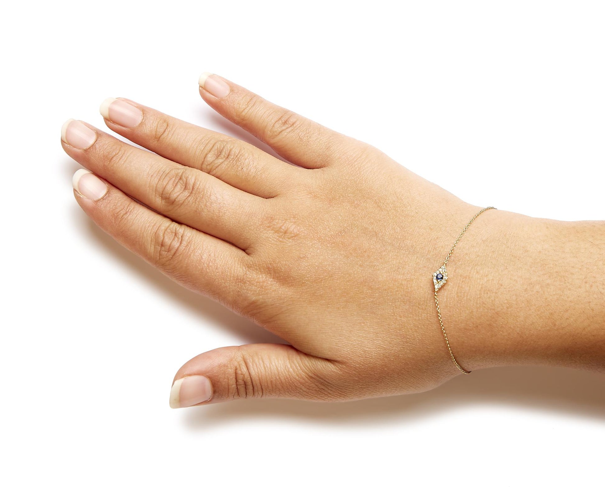 Yellow metal bracelet with a small diamond and blue gemstone cluster on a model's wrist, shown from above at an angle.