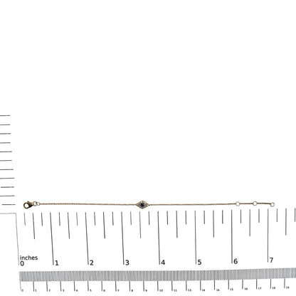 Yellow metal bracelet with a small diamond-shaped centerpiece featuring a blue gemstone surrounded by white gemstones, shown flat on a ruler for size reference, shot from above.