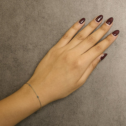 Close-up front angle of a model's wrist wearing a delicate yellow bracelet with a fine chain featuring two round white gemstones and three round green gemstones in bezel settings.