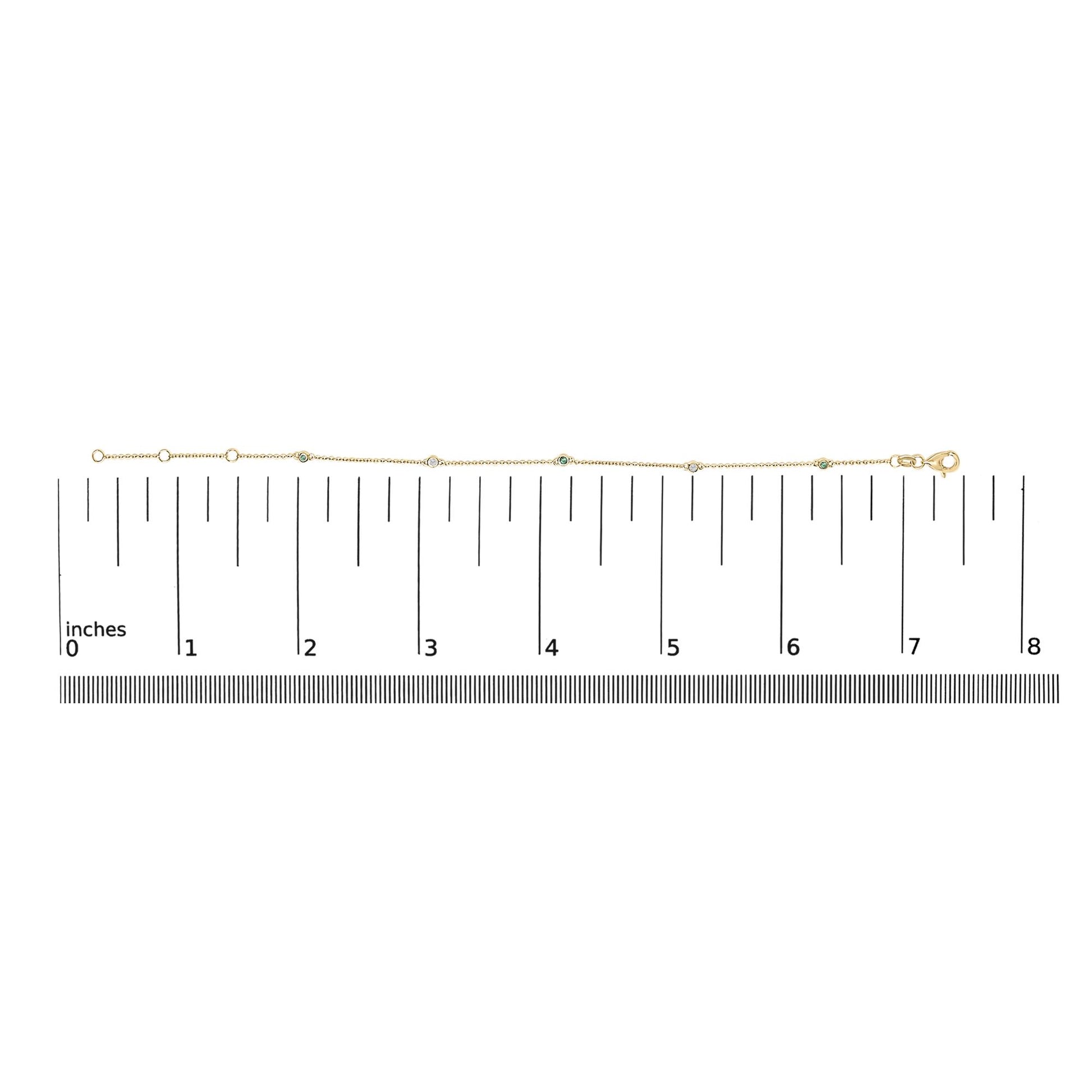 Yellow metal bracelet with round white and green gemstones in bezel settings, shown on a flat surface with a measurement scale, top-down view.