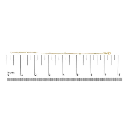 Yellow metal bracelet with round white and green gemstones in bezel settings, shown on a flat surface with a measurement scale, top-down view.