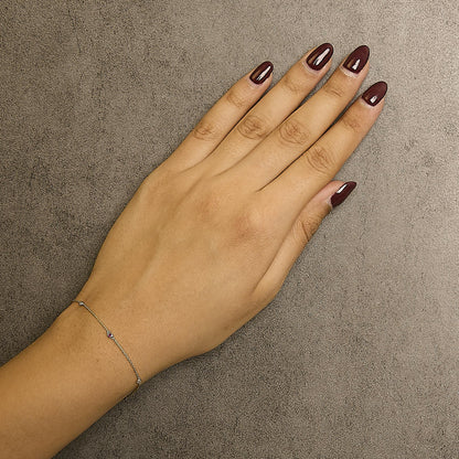 Close-up top view of a yellow metal delicate bracelet with small round red and white gemstones in bezel settings, worn on a model's wrist.