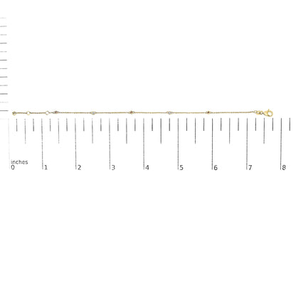 Yellow metal bracelet with alternating round white and red gemstones in bezel settings, shown horizontally on a ruler for size reference.