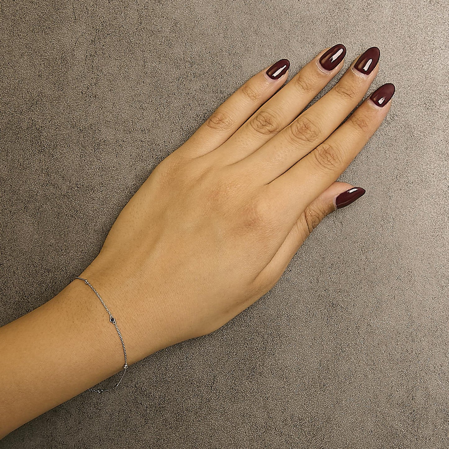 Close-up angled top view of a model's hand wearing a delicate white bracelet with a fine chain and round blue and white gemstones in bezel settings.