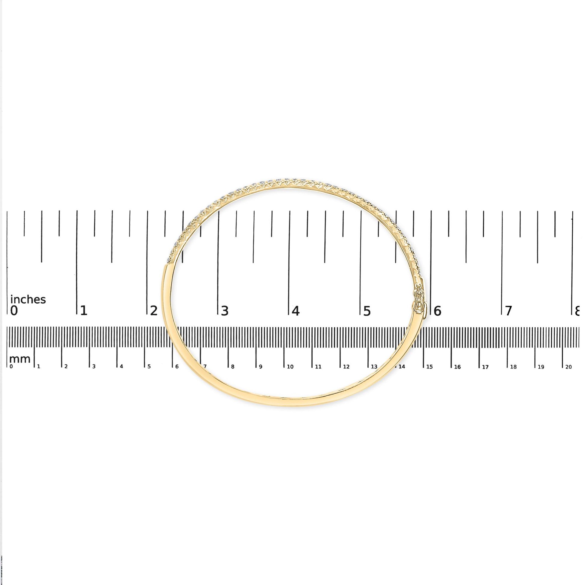 Top-down view of a yellow bracelet with a row of white round pave-set gemstones, placed on a ruler for size reference.