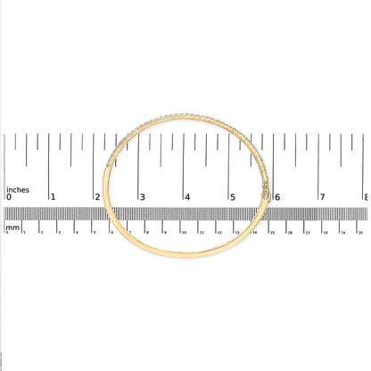 Top-down view of a yellow bracelet with a row of white round pave-set gemstones, placed on a ruler for size reference.