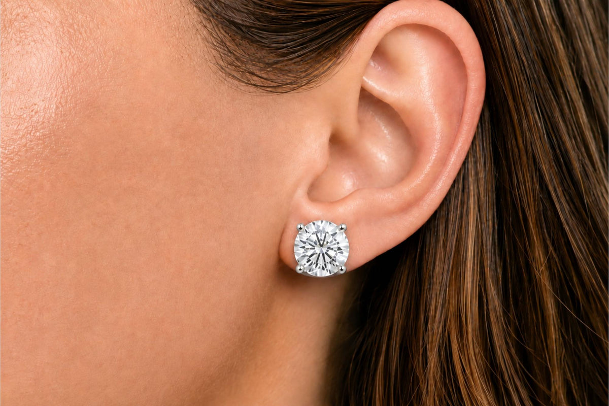 Close-up side view of a model wearing a white metal stud earring with a round white gemstone in a four-prong setting.