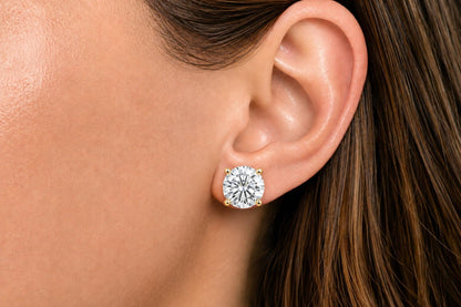 Close-up side view of a model wearing a pair of yellow metal stud earrings with round white gemstones in a four-prong setting.