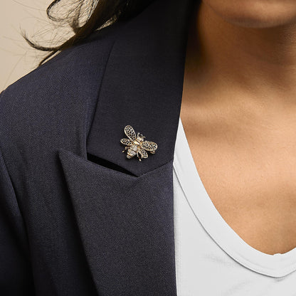Brooch shaped like a bee with yellow and white metal and white round gemstones in prong settings, shown worn on a model's dark blazer lapel, close-up angled view.