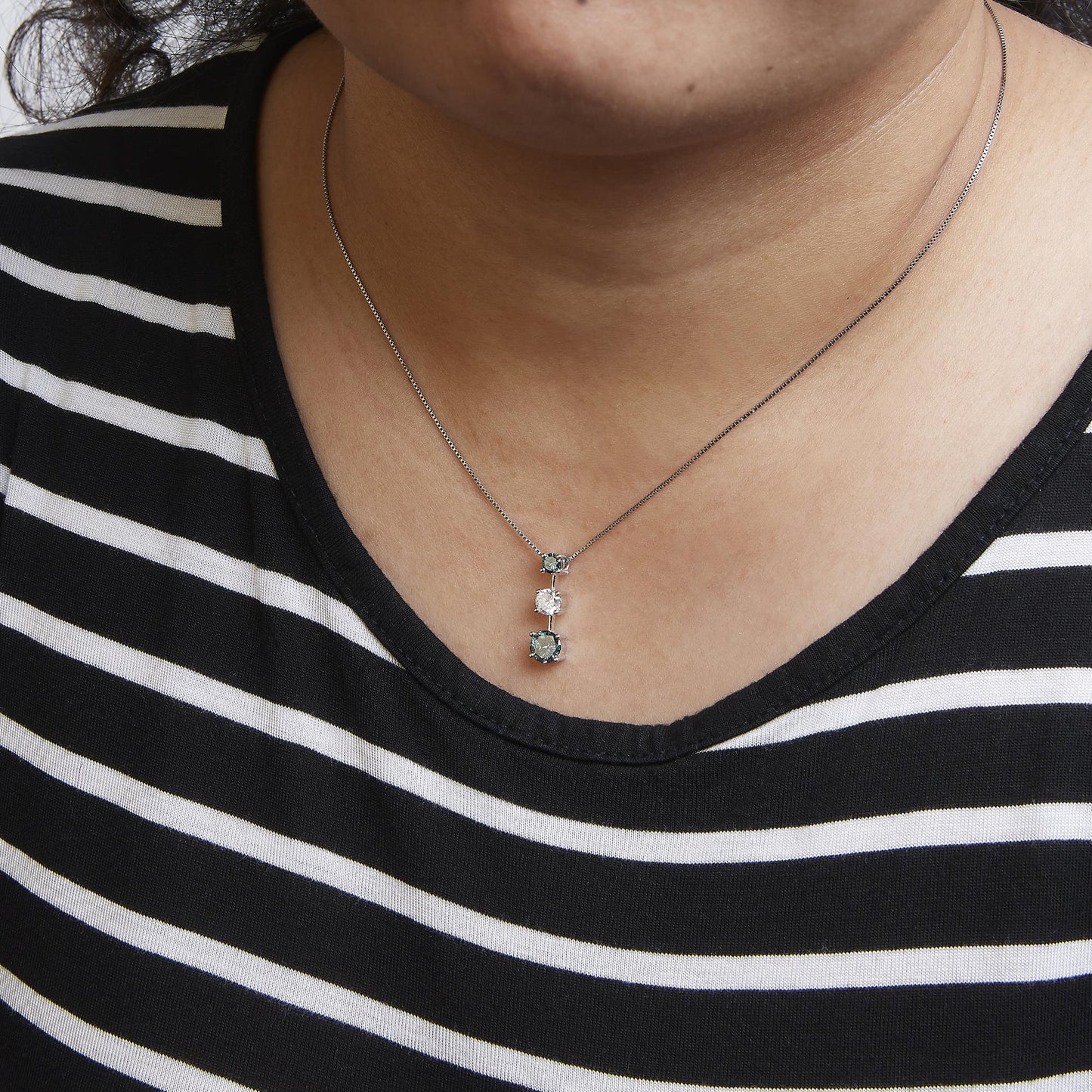 Close-up front view of a white metal necklace on a model, featuring a pendant with one white gemstone flanked by two blue gemstones in prong settings.