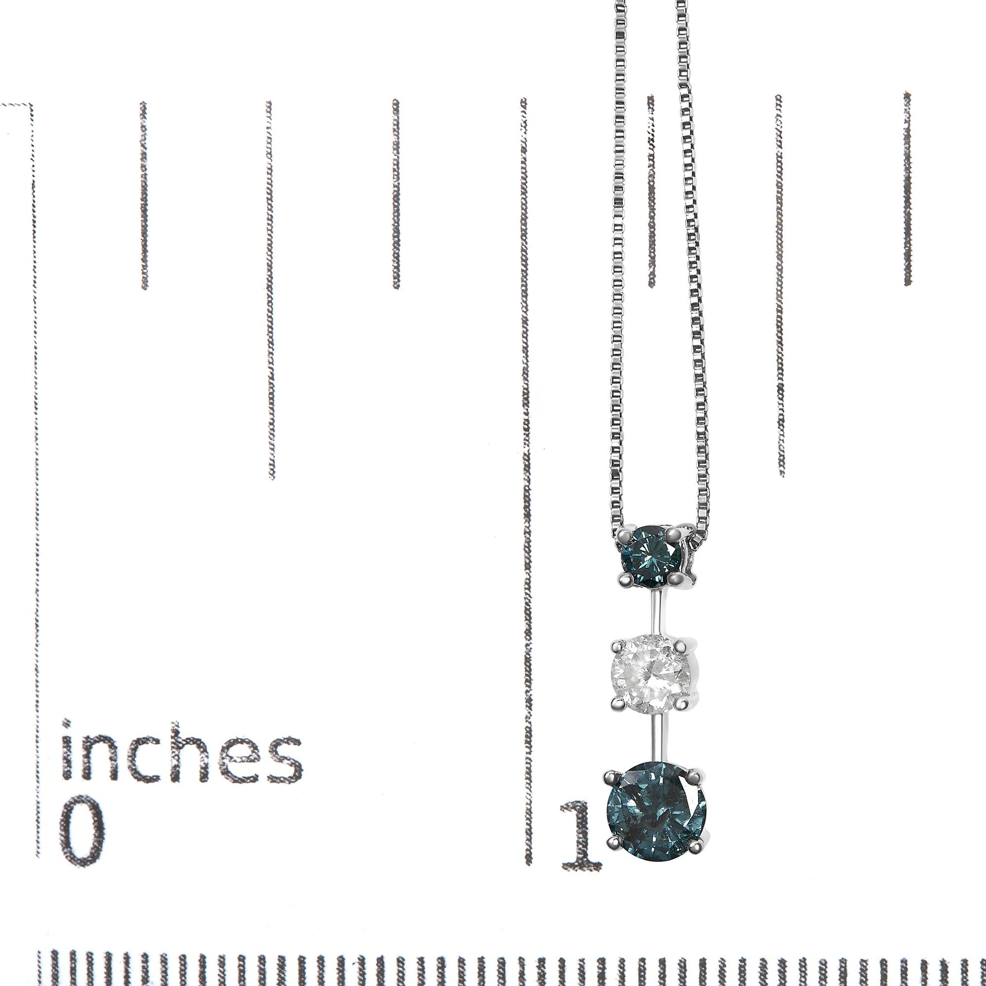 White metal necklace with three round prong-set gemstones, two blue and one white in the center, hanging vertically, photographed on a ruler for size reference.