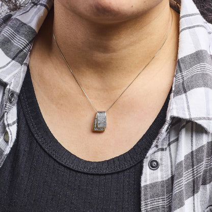 Close-up front view of a necklace with yellow and white metal pendant featuring two overlapping trapezoid shapes adorned with small white gemstones, worn on a model.