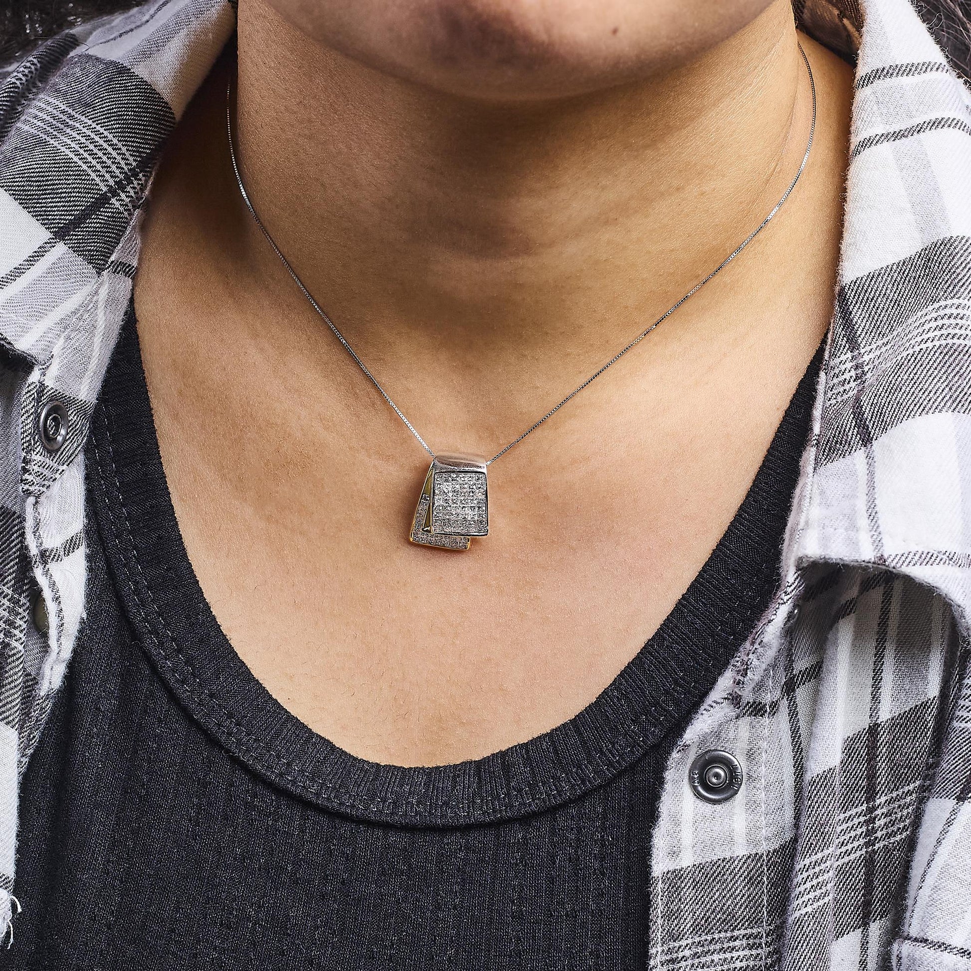 Close-up front view of a necklace with a pendant featuring two overlapping trapezoid shapes adorned with white princess-shaped gemstones in an invisible setting, with a thin yellow and white metal chain.