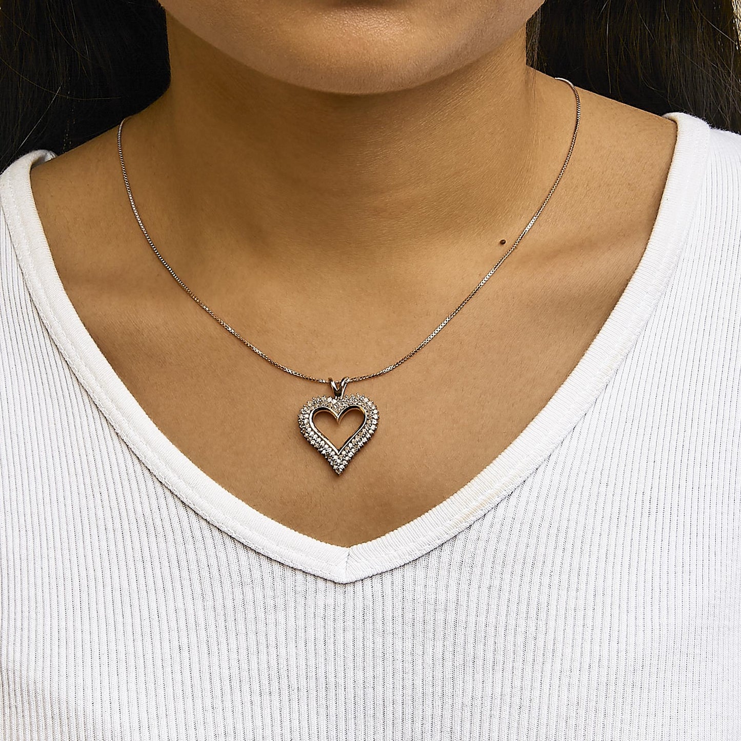 Close-up front view of a rose-colored heart-shaped necklace pendant with white round gemstones in prong settings, worn on a model.